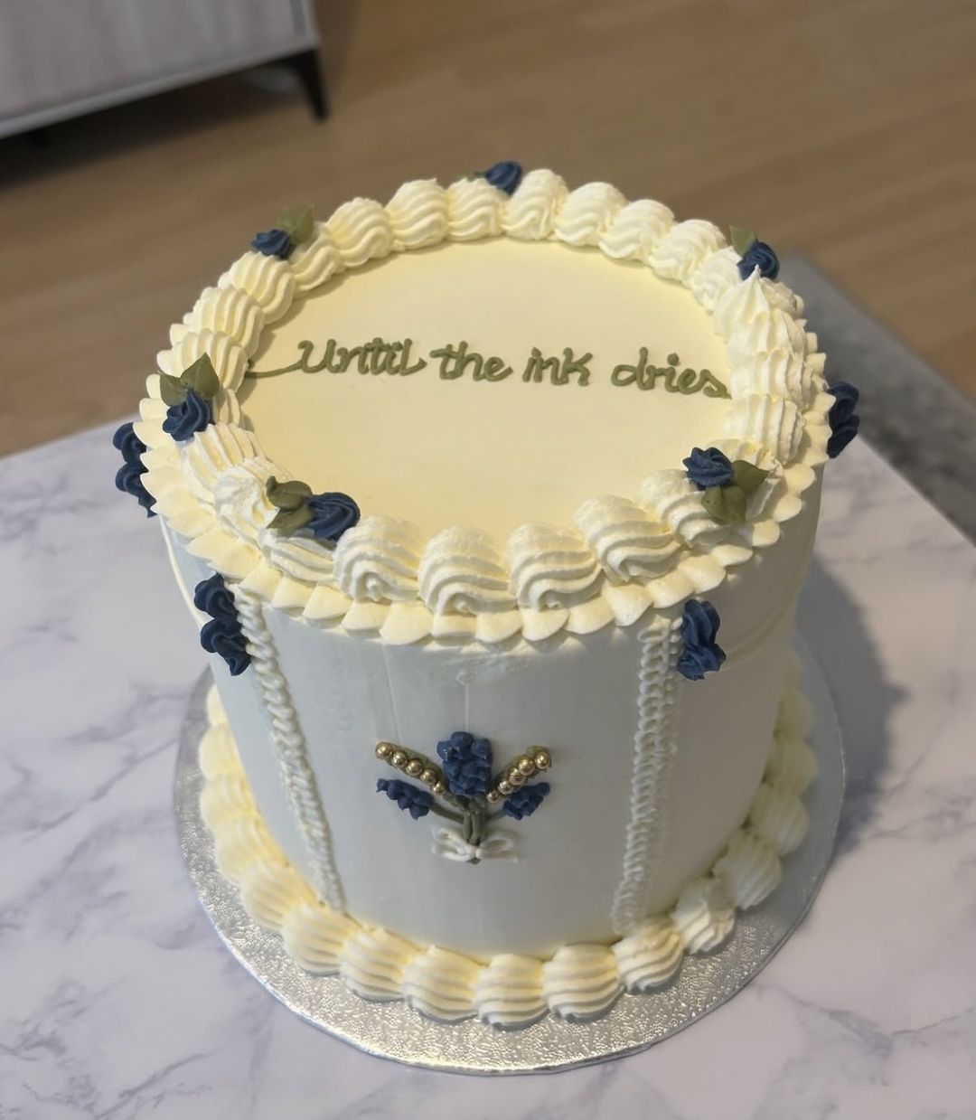 Tall white cake with blue piped flower bouquets, ivory borders and “Until the ink dries” on top (photo 2 of 2)